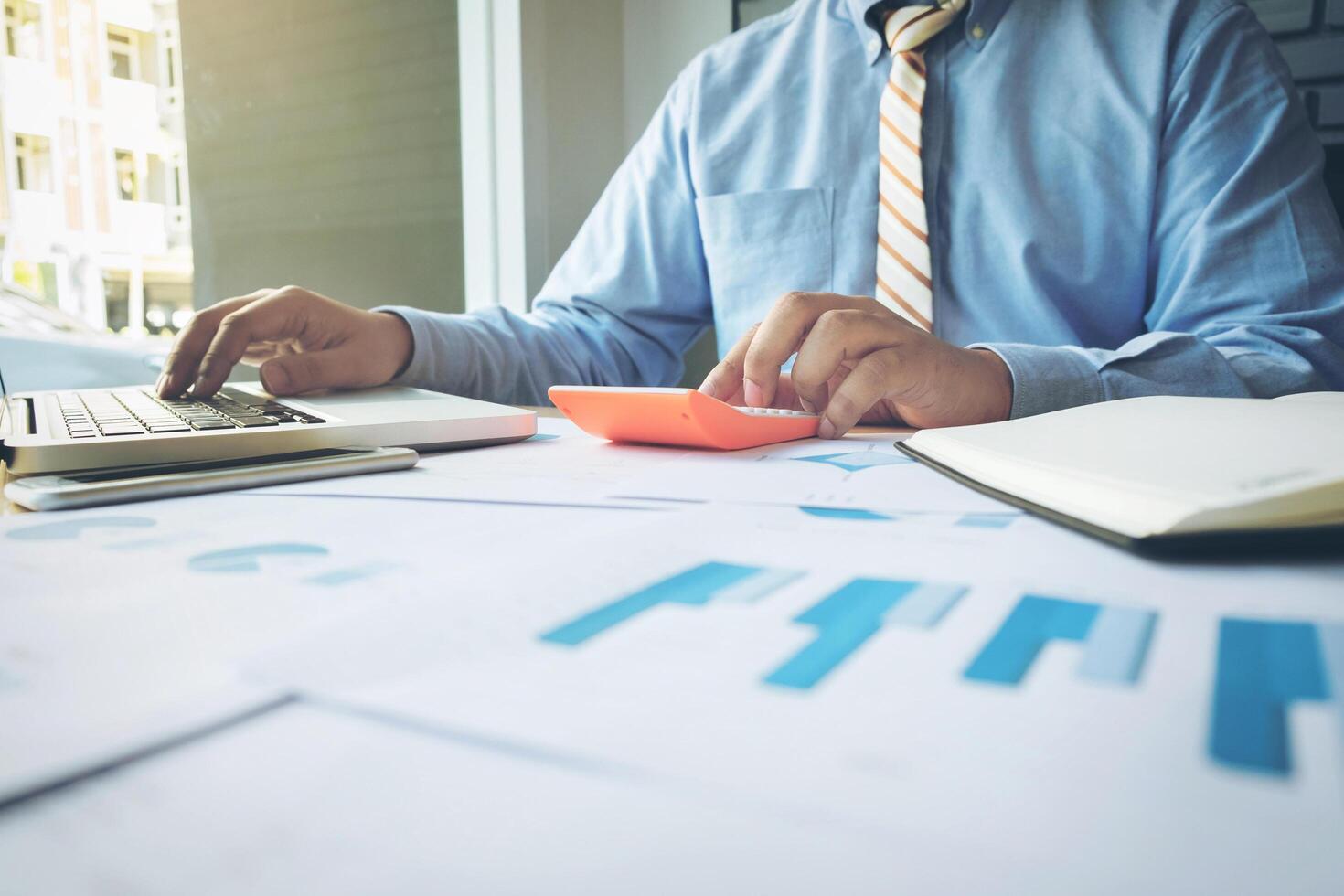 Handsome young businessman working with laptop while sitting on the desk in office and financial statistic graph photo