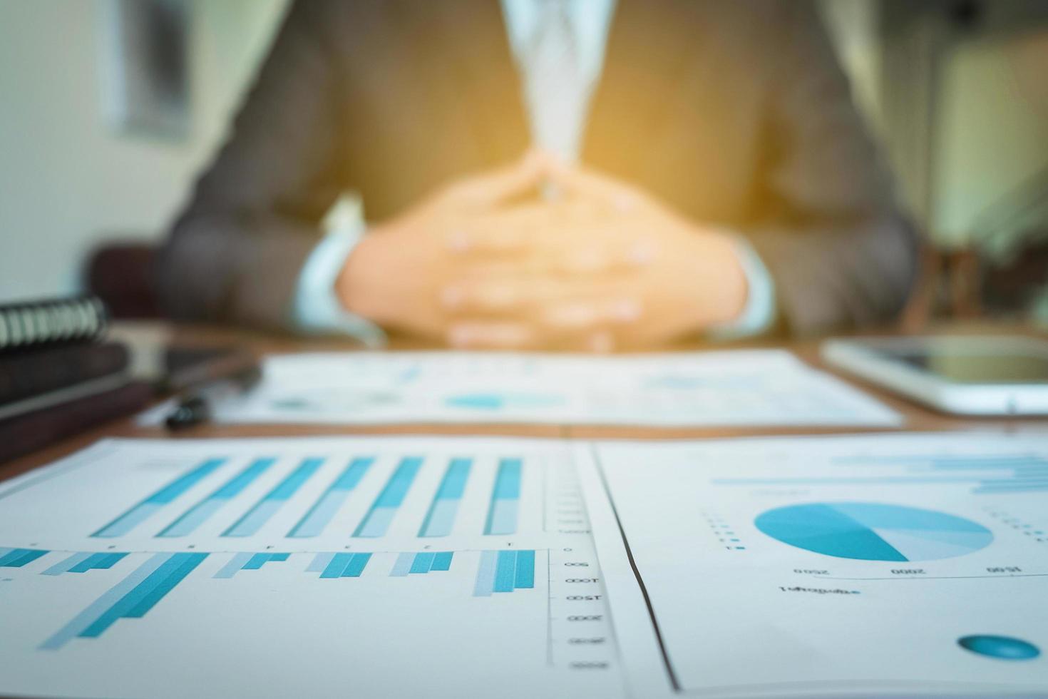 business documents on office table with graph financial diagram and businessman working in the background, business concept. photo