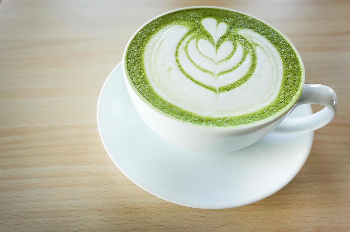 matcha green tea latte with heart shape latte art in white cup on wooden table photo