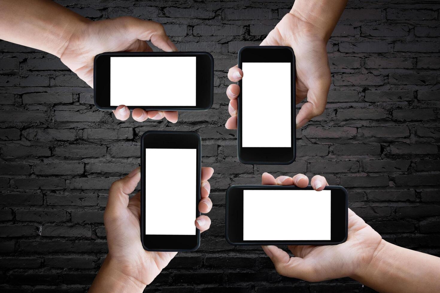 four hands holding horizontal the black smartphone with blank screen, old brick wall background. photo