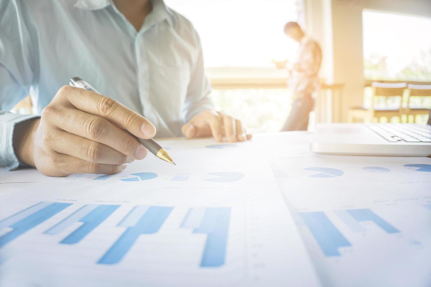Handsome young businessman working with laptop while sitting on the desk in office and financial statistic graph. photo