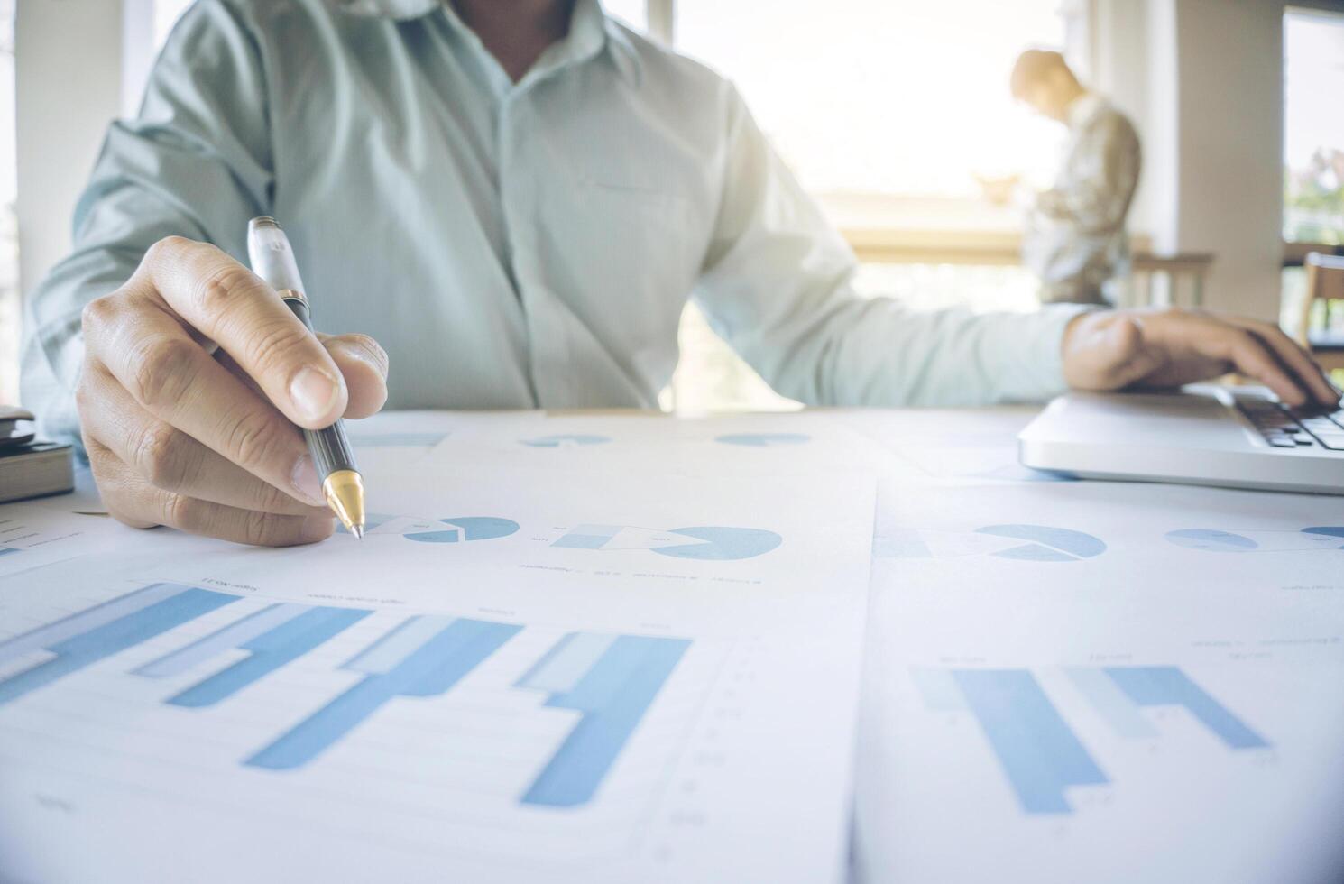 Handsome young businessman working with laptop while sitting on the desk in office and financial statistic graph photo