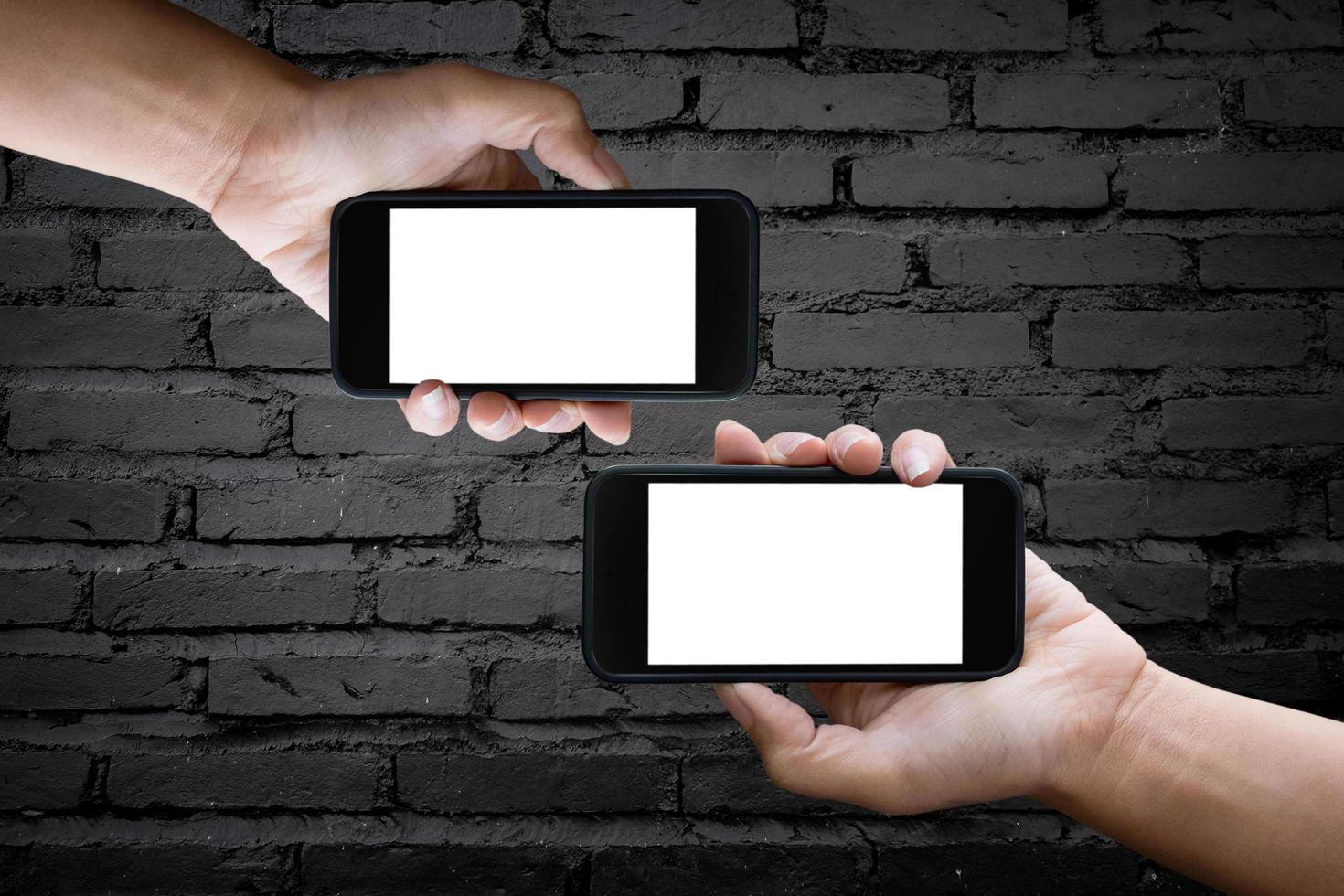 Two hands holding blank screen of a smartphone at the old black brick wall. photo