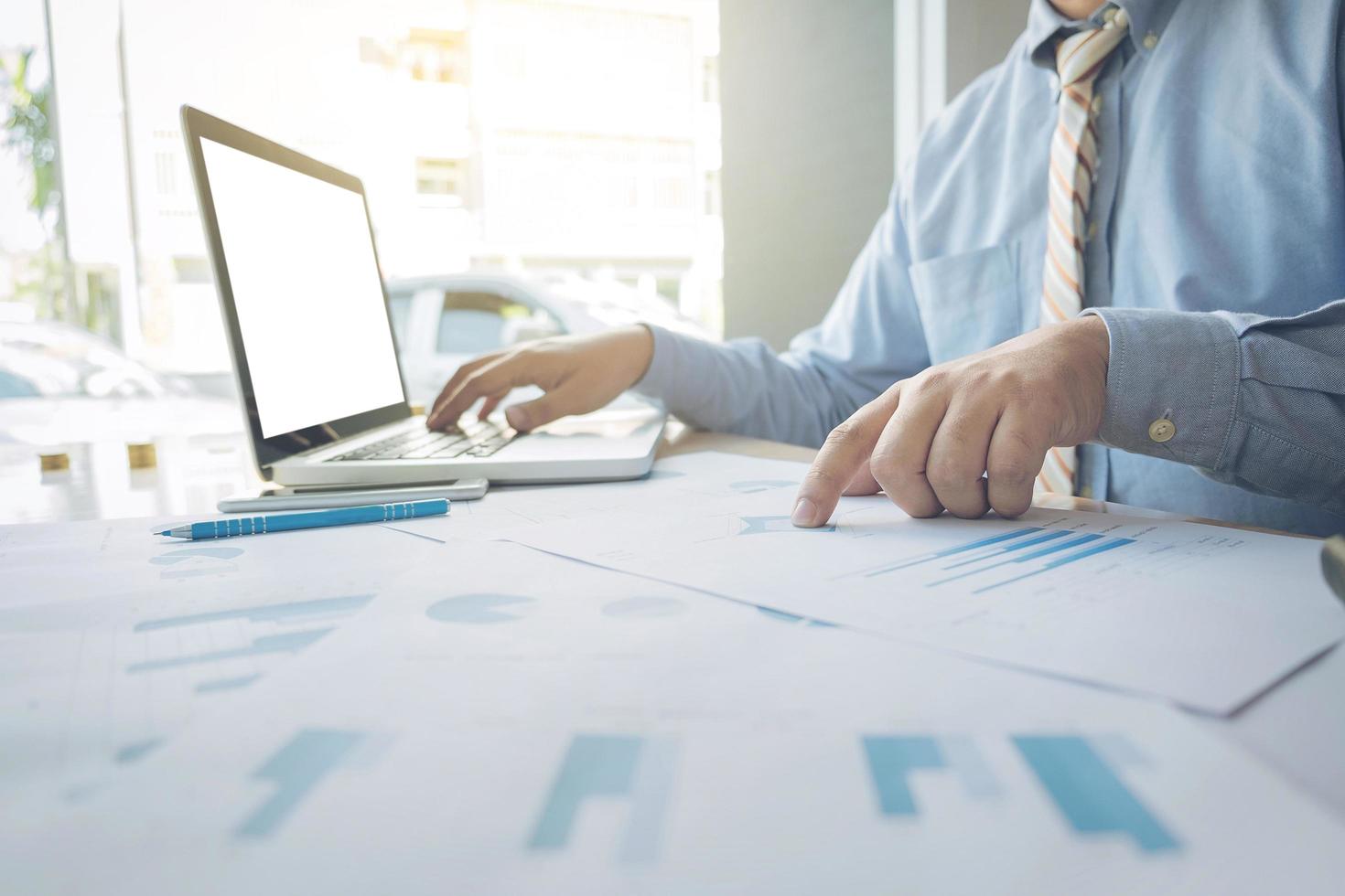 Handsome young businessman working with laptop while sitting on the desk in office and financial statistic graph photo