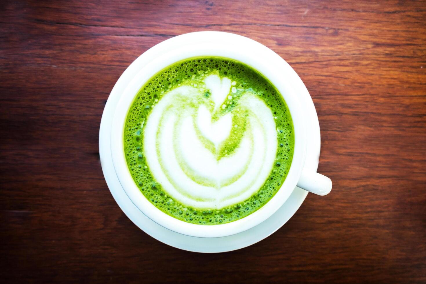 matcha green tea latte with heart shape latte art in white cup on wooden table. Top view photo