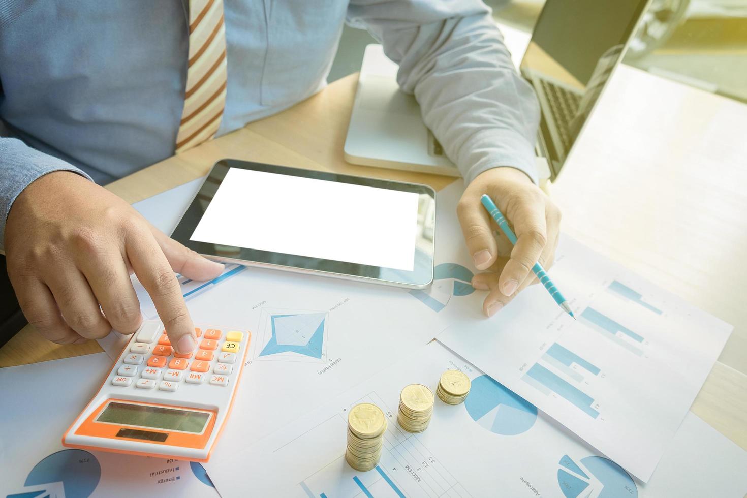 businessman using calculator with stacked coins arranged at office desk and many document data graph in morning light, business concept. photo