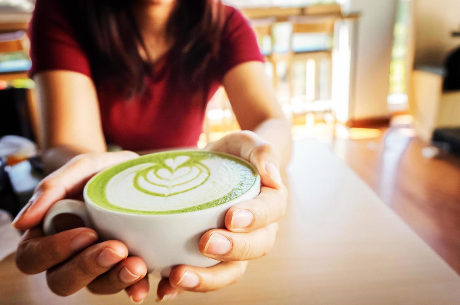 Woman holding cup of hot matcha green tea in her hands, sitting in the coffee shop in the morning photo