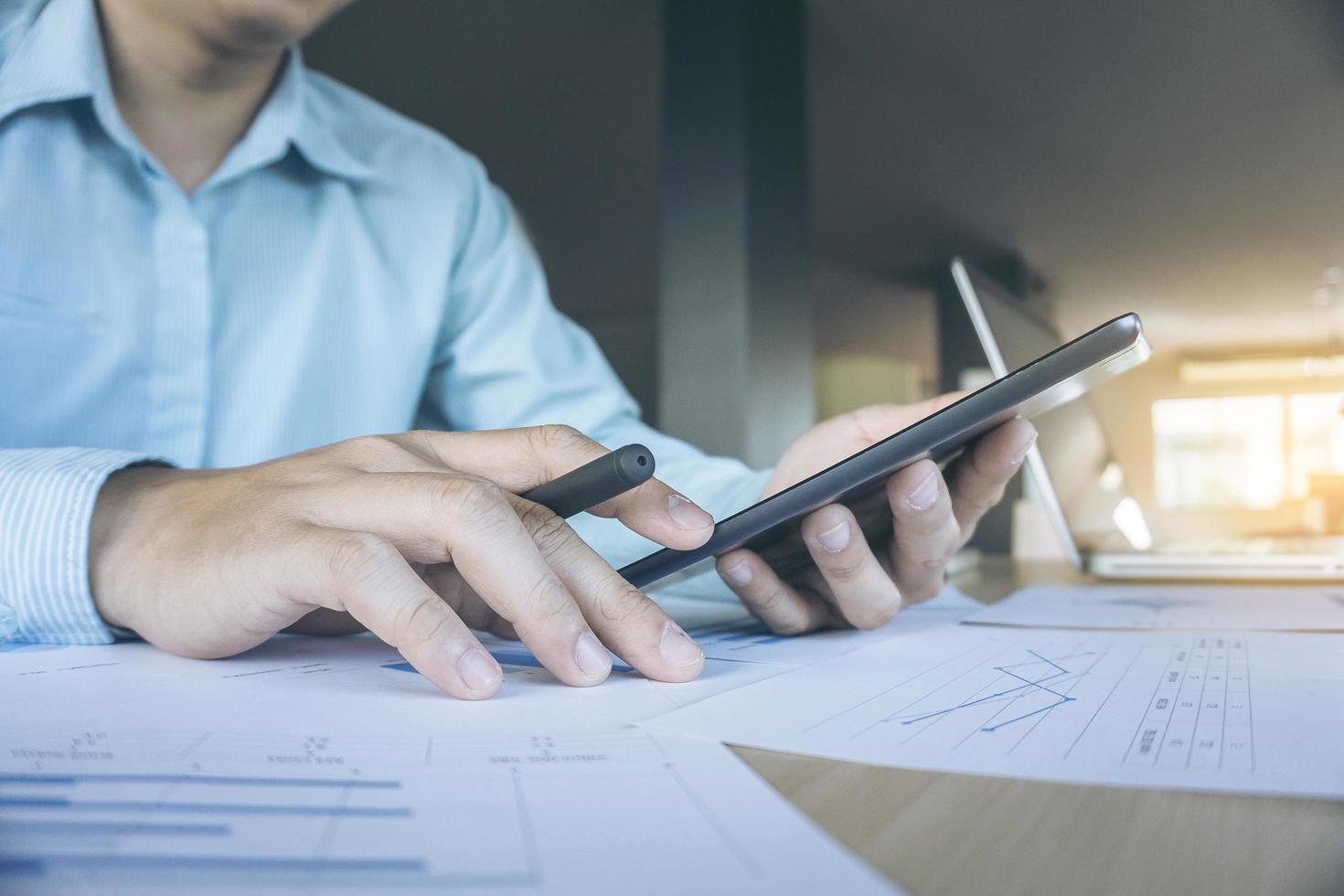 Closeup shot of business man's hands using tablet with many document graph and laptop in morning photo