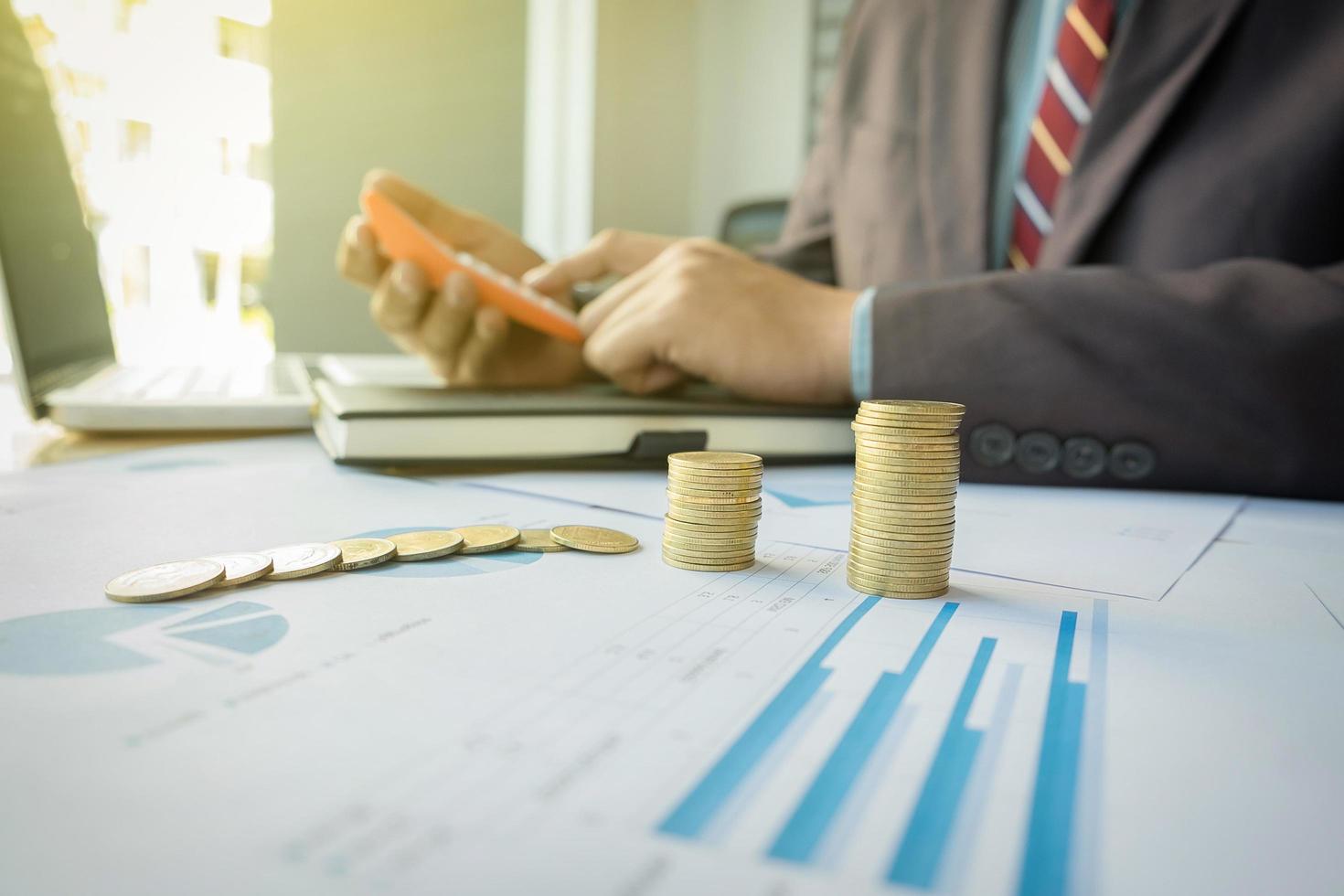 businessman using calculator with stacked coins arranged at office desk and many document data graph in morning light, business concept. photo