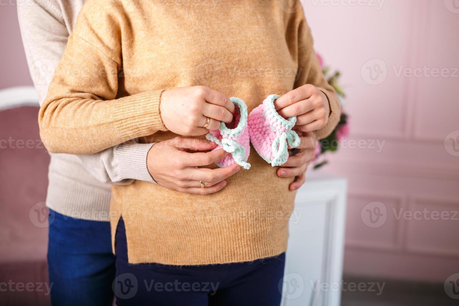 knitted booties in the hands of a pregnant woman next to her husband. waiting for a miracle photo