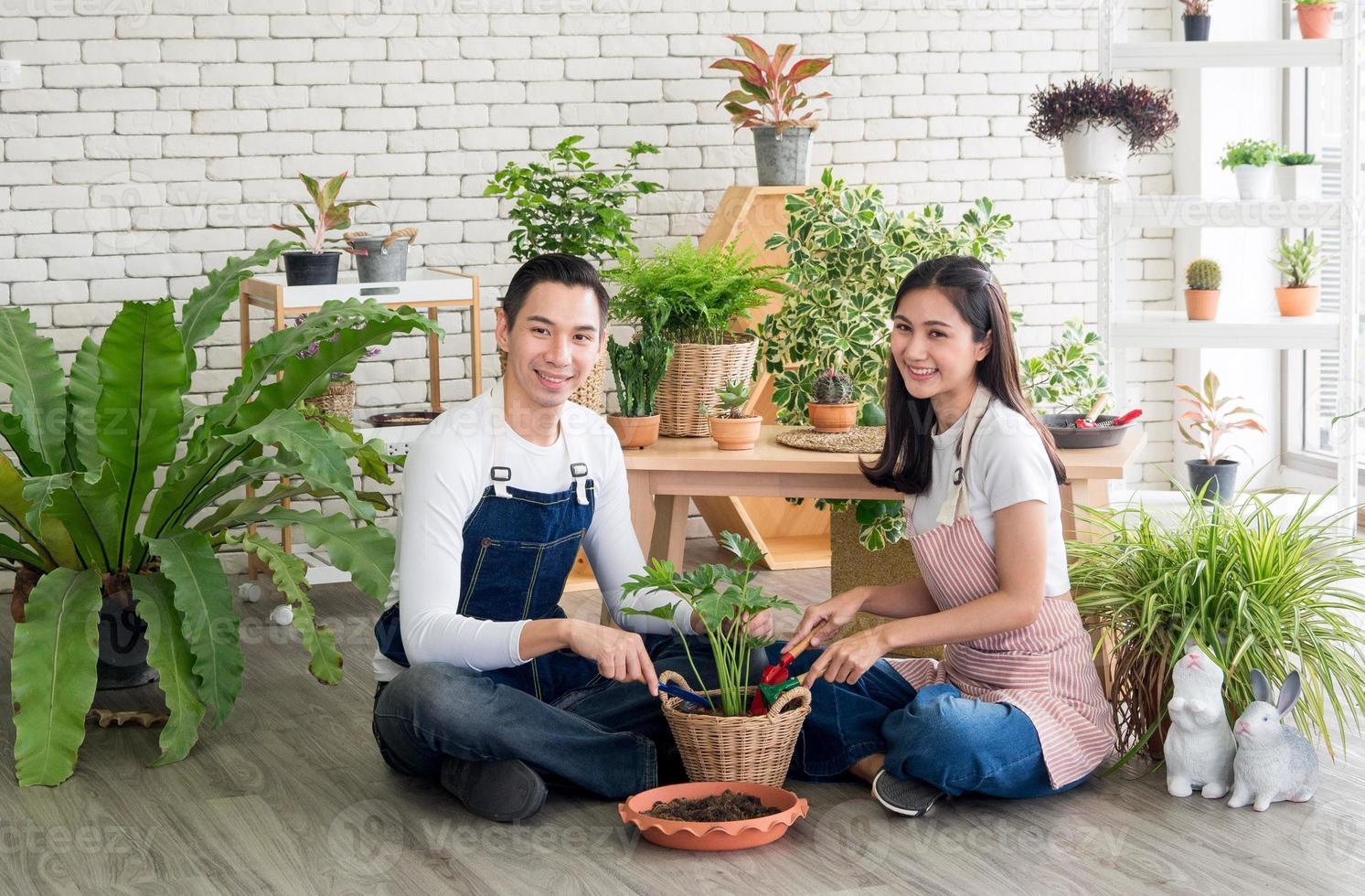 gardener young Asian man woman two person sitting with floor smiling looking hand holding basket pot small tree leaf green in calm work shop home plant white wall. hobby job happy and care concept photo