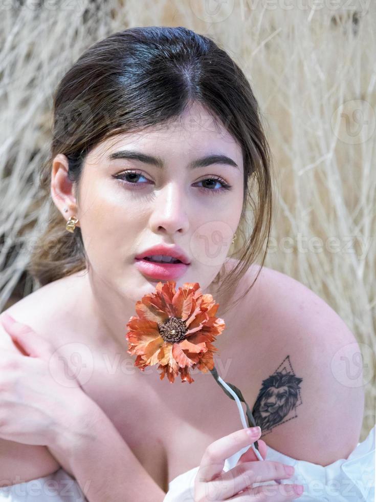 retrato joven hermosa niña mujer bastante encantadora cara makup camisa blanca con cabello largo sonriendo sentada mano sosteniendo flor seca atractiva mirando sonrisa, feliz y brillante disfrutar en la habitación de casa. foto