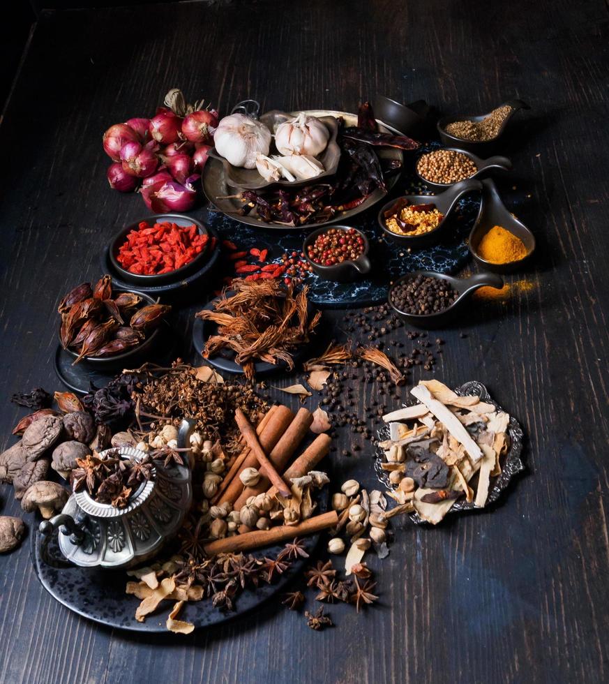 Top view photo Lots of garlic, onions, peppers, chili and dried herbs, were placed on plates and cups on a black wooden drak background. was divided To prepare to cook food india healthy food