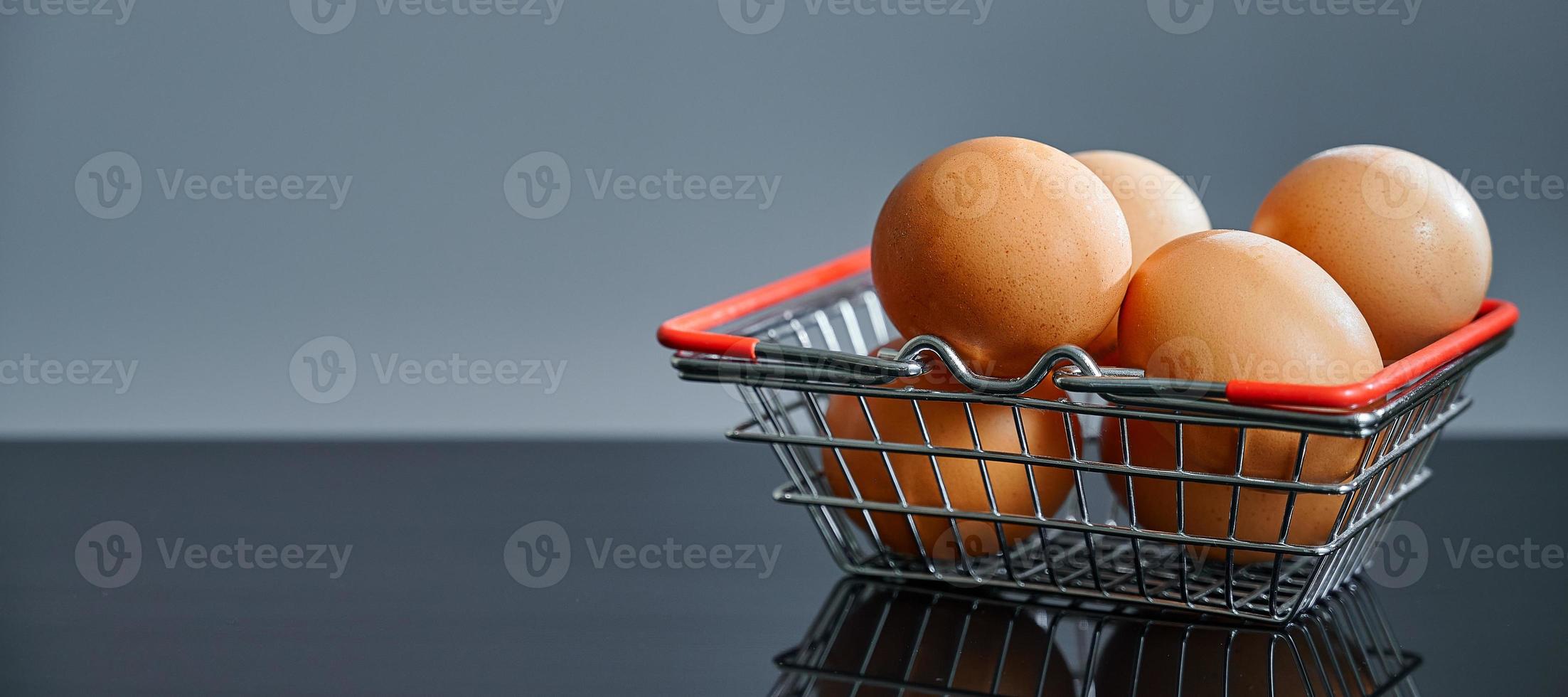 Eggs in the shopping basket on a black table with a reflection. Brown eggs in the basket. Photo with copy space.