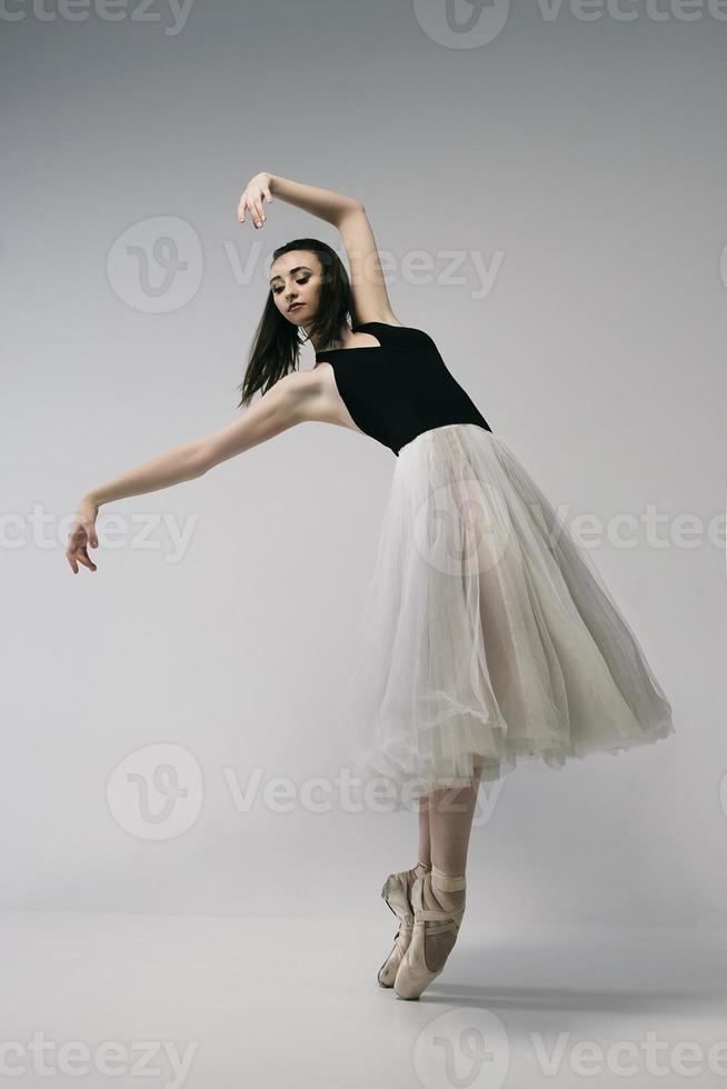 ballerina in a bodysuit and a white skirt improvises classical and modern choreography in a photo studio