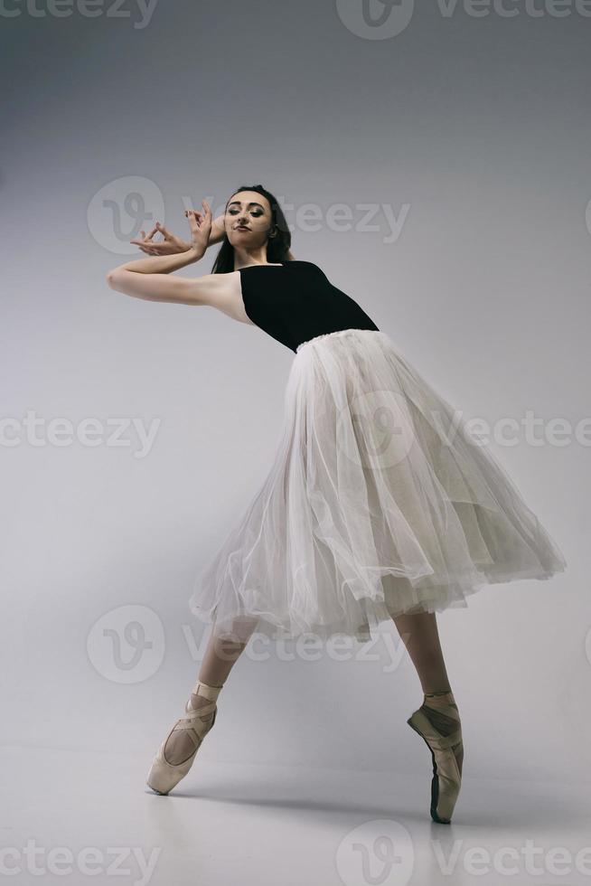 ballerina in a bodysuit and a white skirt improvises classical and modern choreography in a photo studio