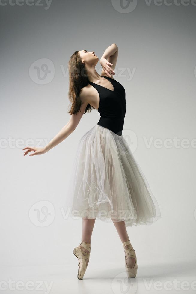 ballerina in a bodysuit and a white skirt improvises classical and modern choreography in a photo studio