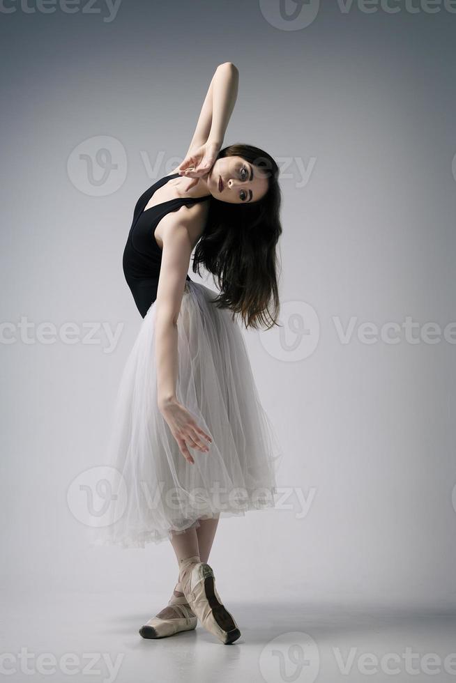 a ballerina in a bodysuit and a white skirt improvises classical and modern choreography in a photo studio