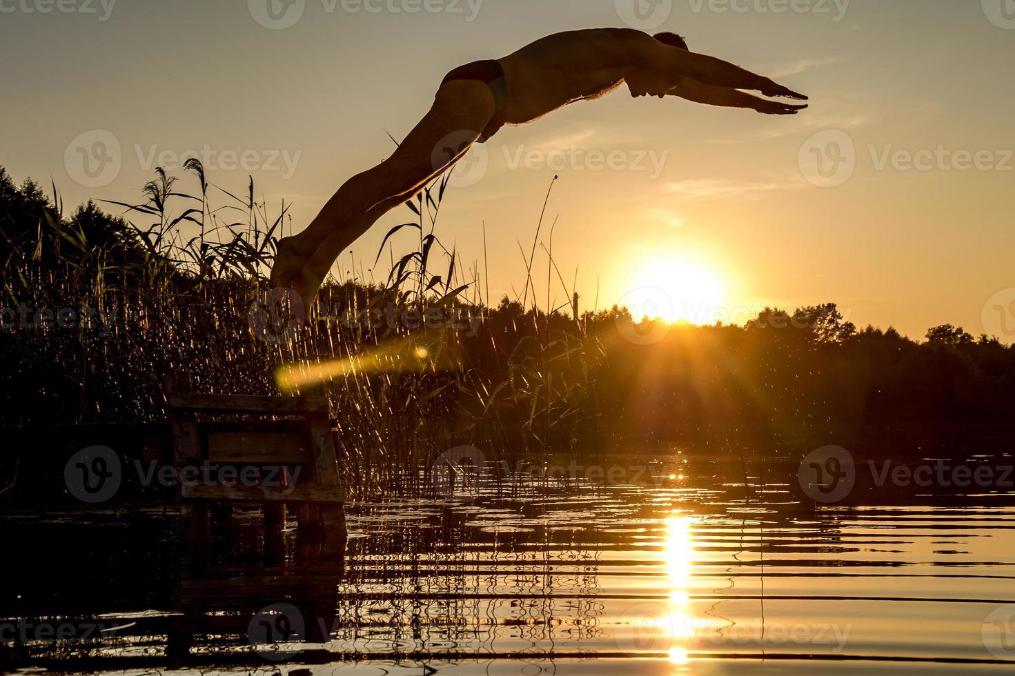 man dives into the water of lake at sunset photo