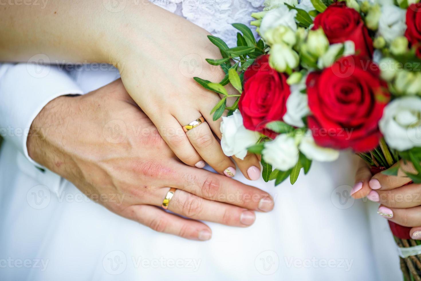 groom embraces the bride with wedding red white rose bouquet. rings on the hands of newly-married couple photo