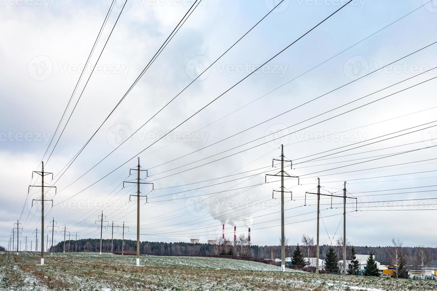 Silhouette of the high voltage electric pylon towers on the background of beautiful clouds. steaming pipes of a thermal power plant photo