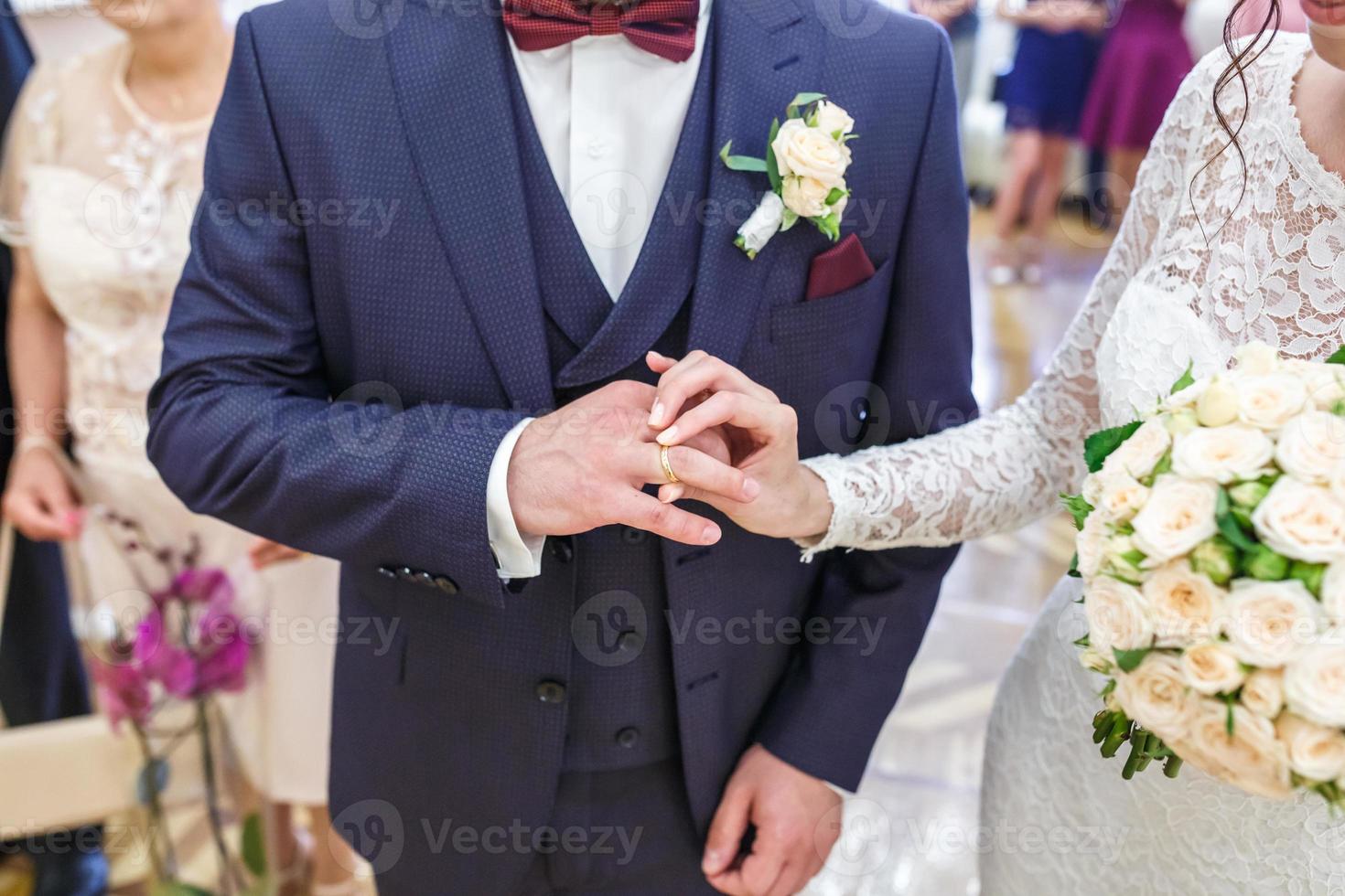 groom embraces the bride with wedding bouquet with violet rose . groom dresses an engagement ring to the bride. newlyweds exchange wedding rings photo