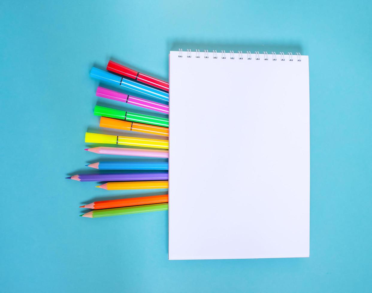 Sketchbook with pencils and felt-tip pens on a blue table. photo