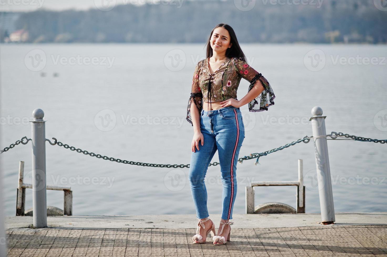 Pretty latino model girl from Ecuador wear on jeans posed against lake. photo