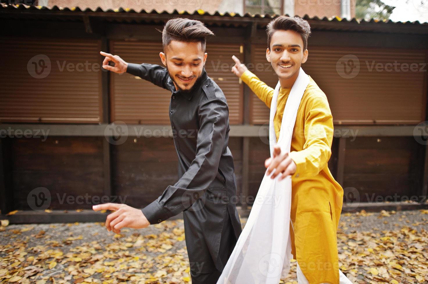 Two indian stylish mans friends in traditional clothes dancing outdoor. Navaratri dance. photo