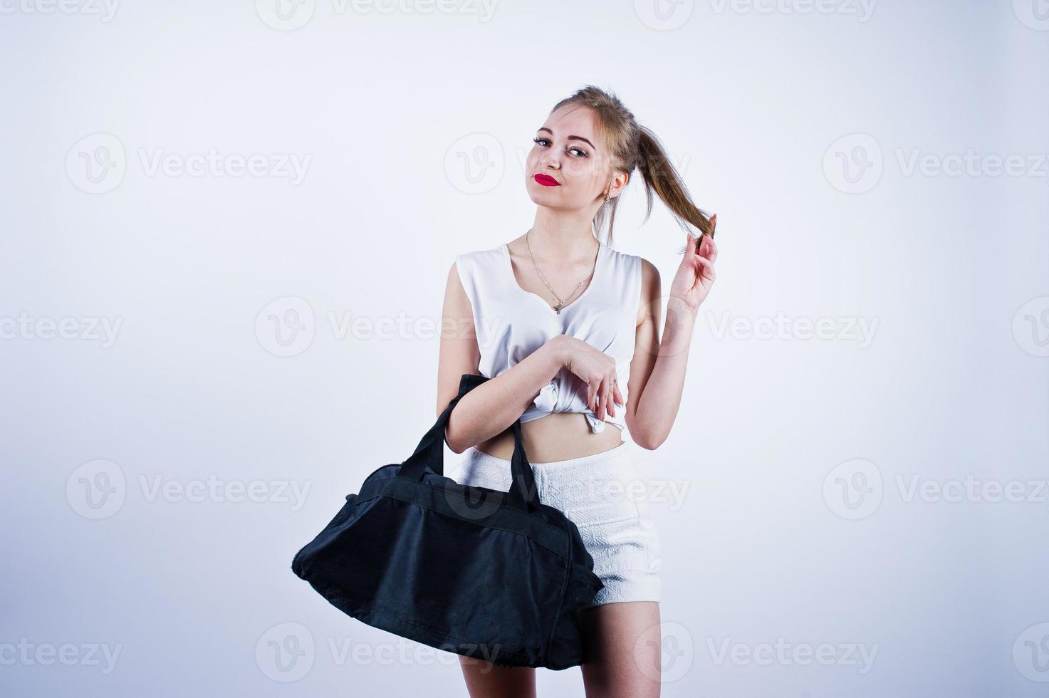 Amazing fit sexy body brunette caucasian girl posing at studio against white background on shorts and top with black sport bag. photo