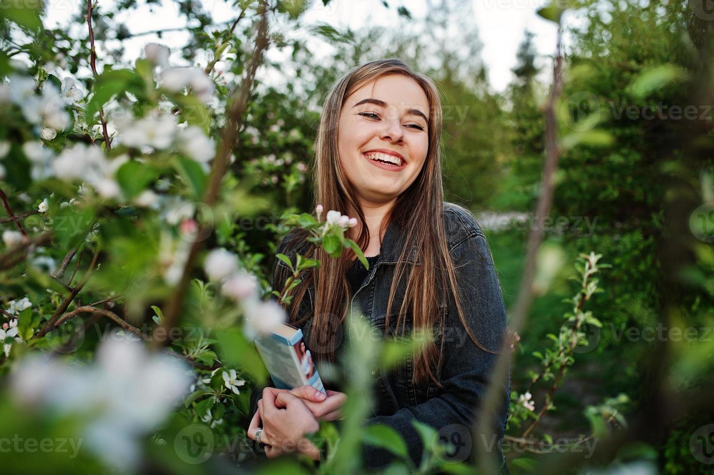 Young brunette girl at jeans against spring blossom tree with book. photo