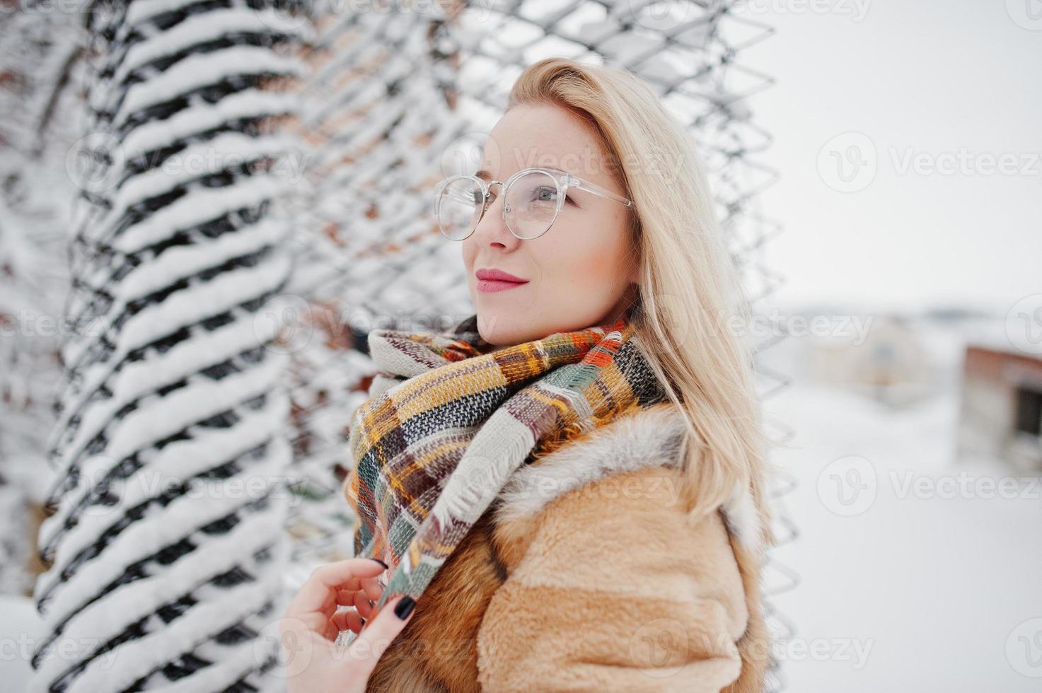 Portraiy of blonde girl in glasses, red fur coat and scarf at winter day. photo