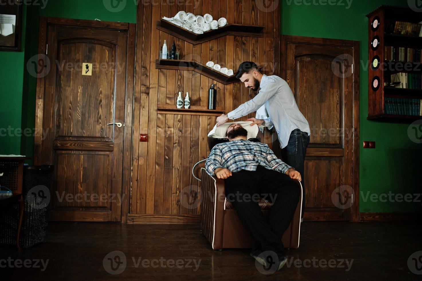 apuesto hombre barbudo en la barbería, peluquero en el trabajo. cabezal de lavado. foto