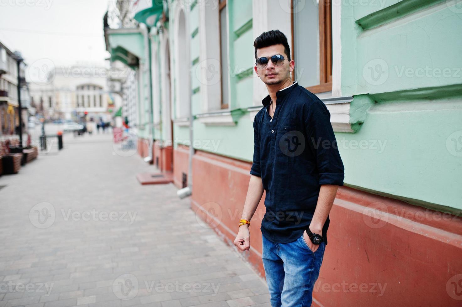 Stylish indian model man in casual clothes, black shirt and sunglasses posed outdoor at street of India. photo