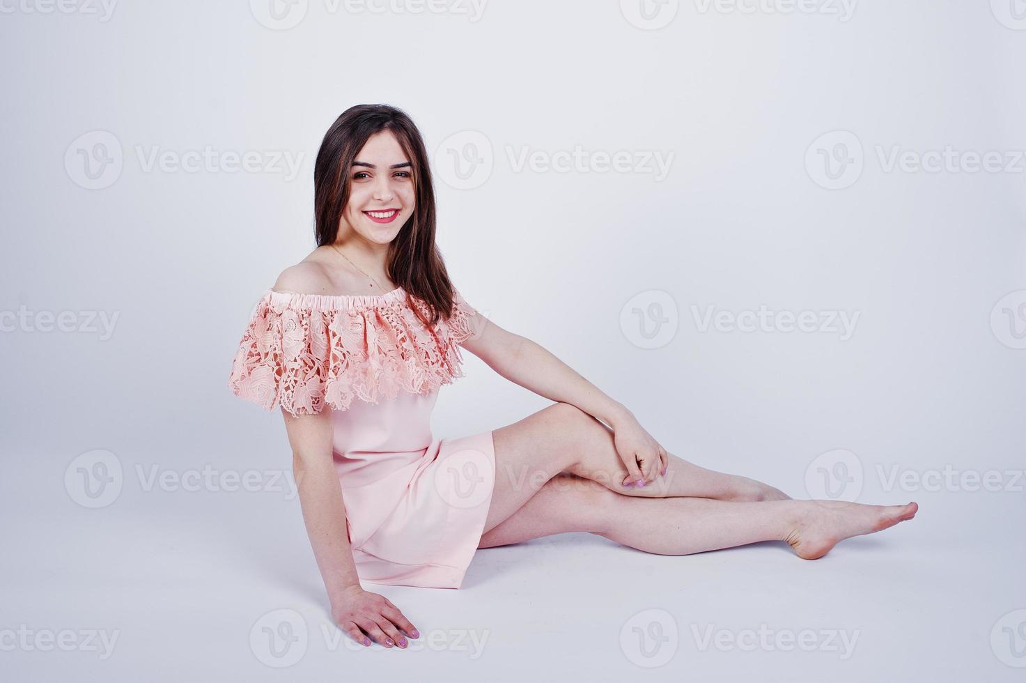 Portrait of a fashionable woman in pink dress sitting and posing on the floor in the studio. photo