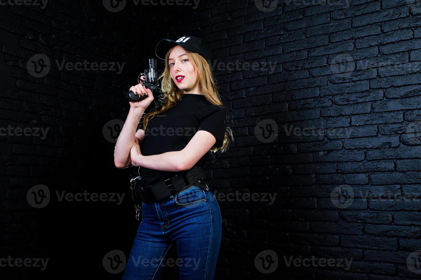 FBI female agent in cap and with gun at studio against dark brick wall. photo