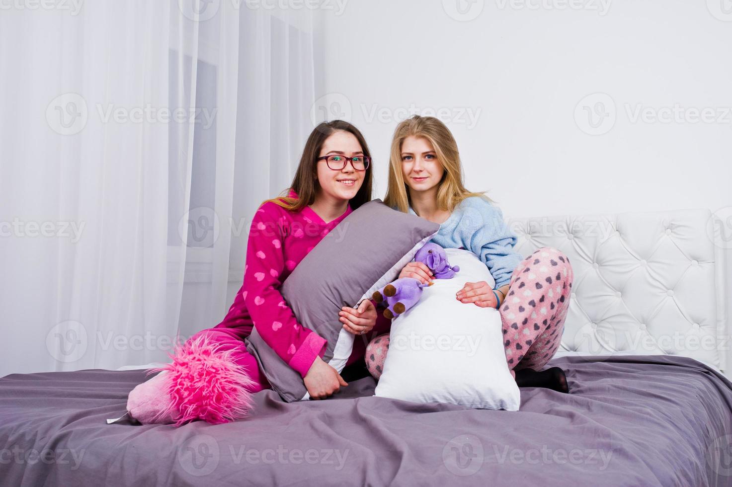 Two friends girls in pajamas having fun on bed at room. photo