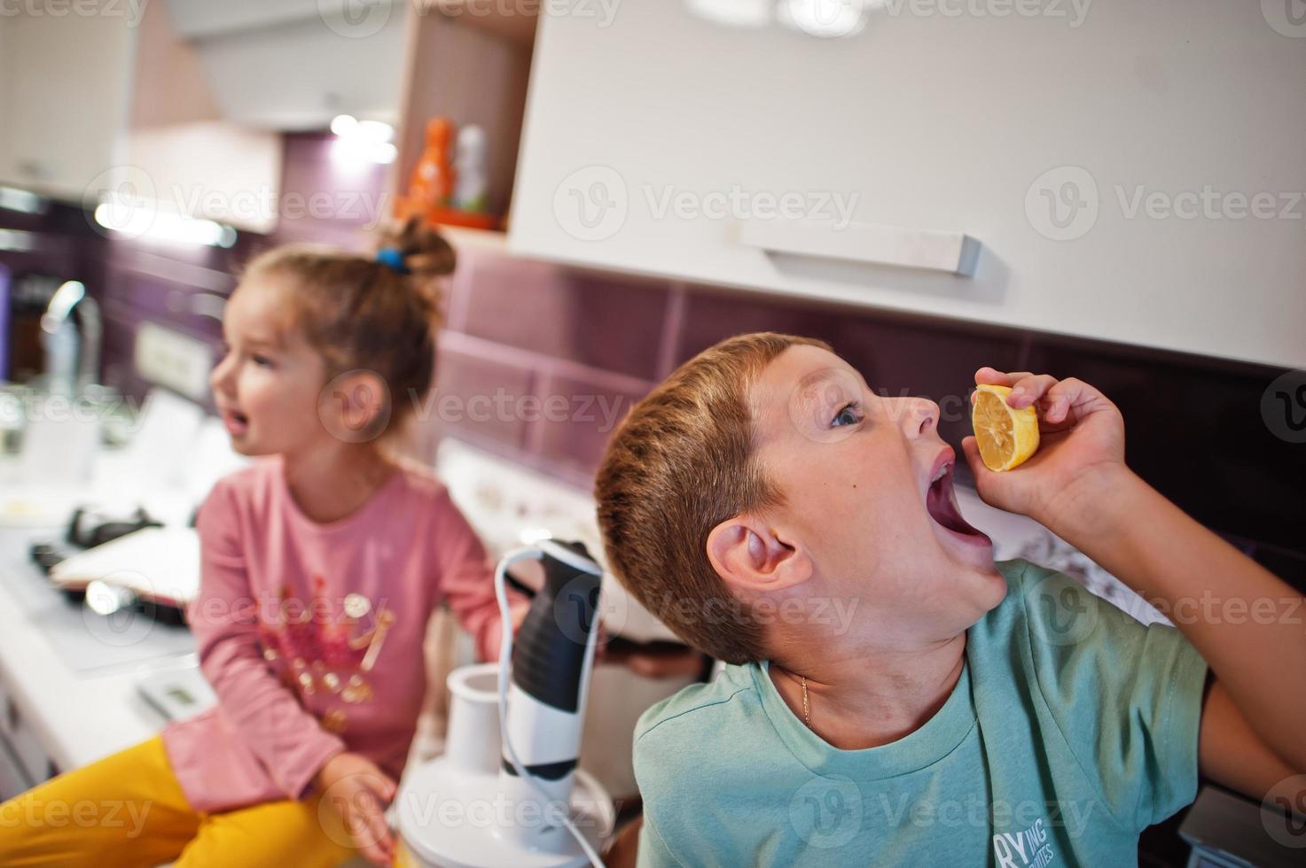 Kids cooking at kitchen, happy children's moments.  Boy eat a lemon. photo