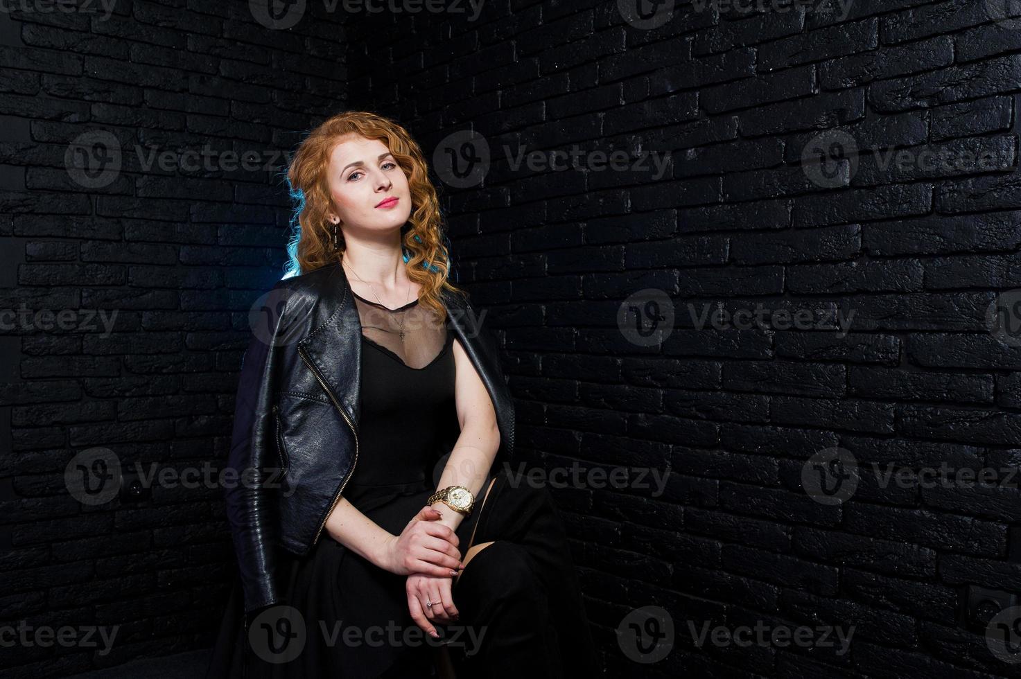 Curly hair girl at leather jacket on studio against black brick wall. photo