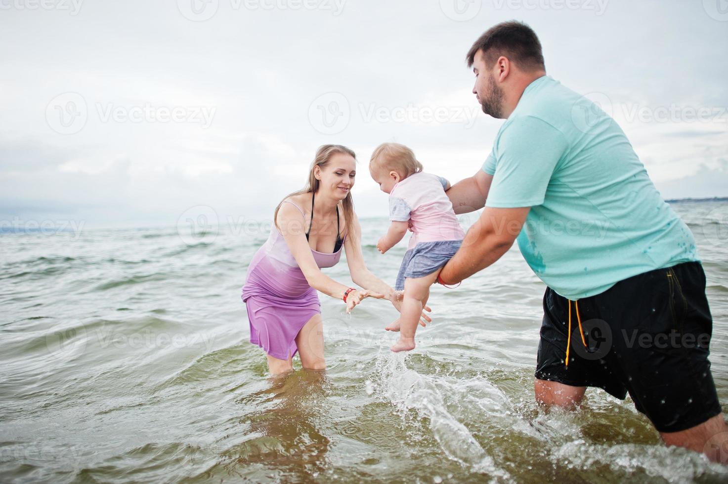 Summer vacations. Parents and people outdoor activity with children. Happy family holidays. Father, pregnant mother, baby daughter on sea sand beach. photo