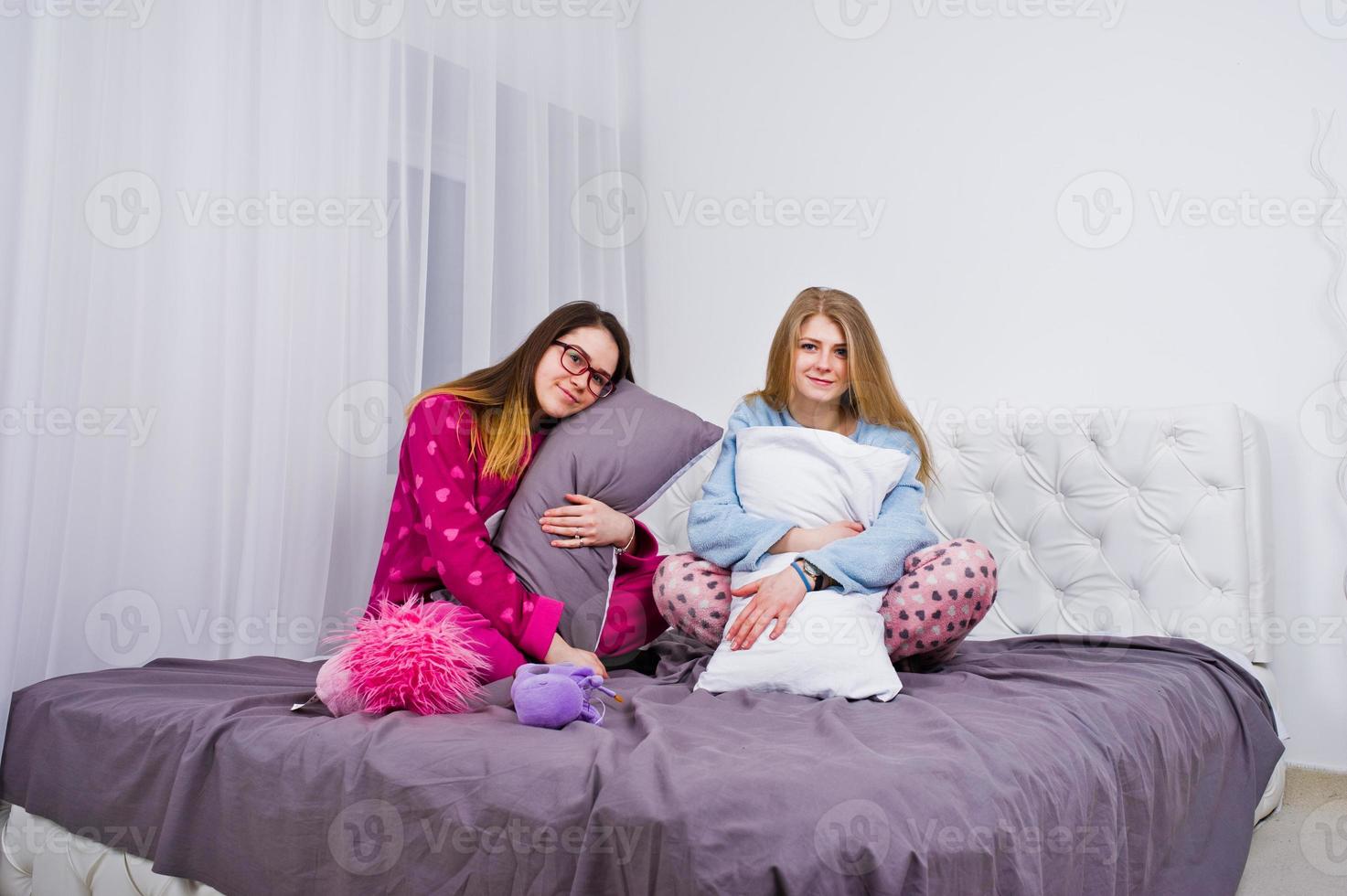 Two friends girls in pajamas having fun on bed at room. photo