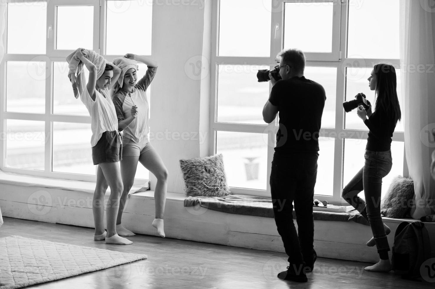 el equipo de dos fotógrafos fotografiando a niñas modelos gemelas en el estudio contra grandes ventanales. fotógrafo profesional en el trabajo. foto