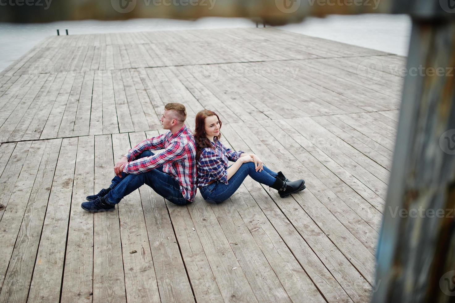 elegante pareja vestida con camisa a cuadros enamorada sentada en el muelle. foto