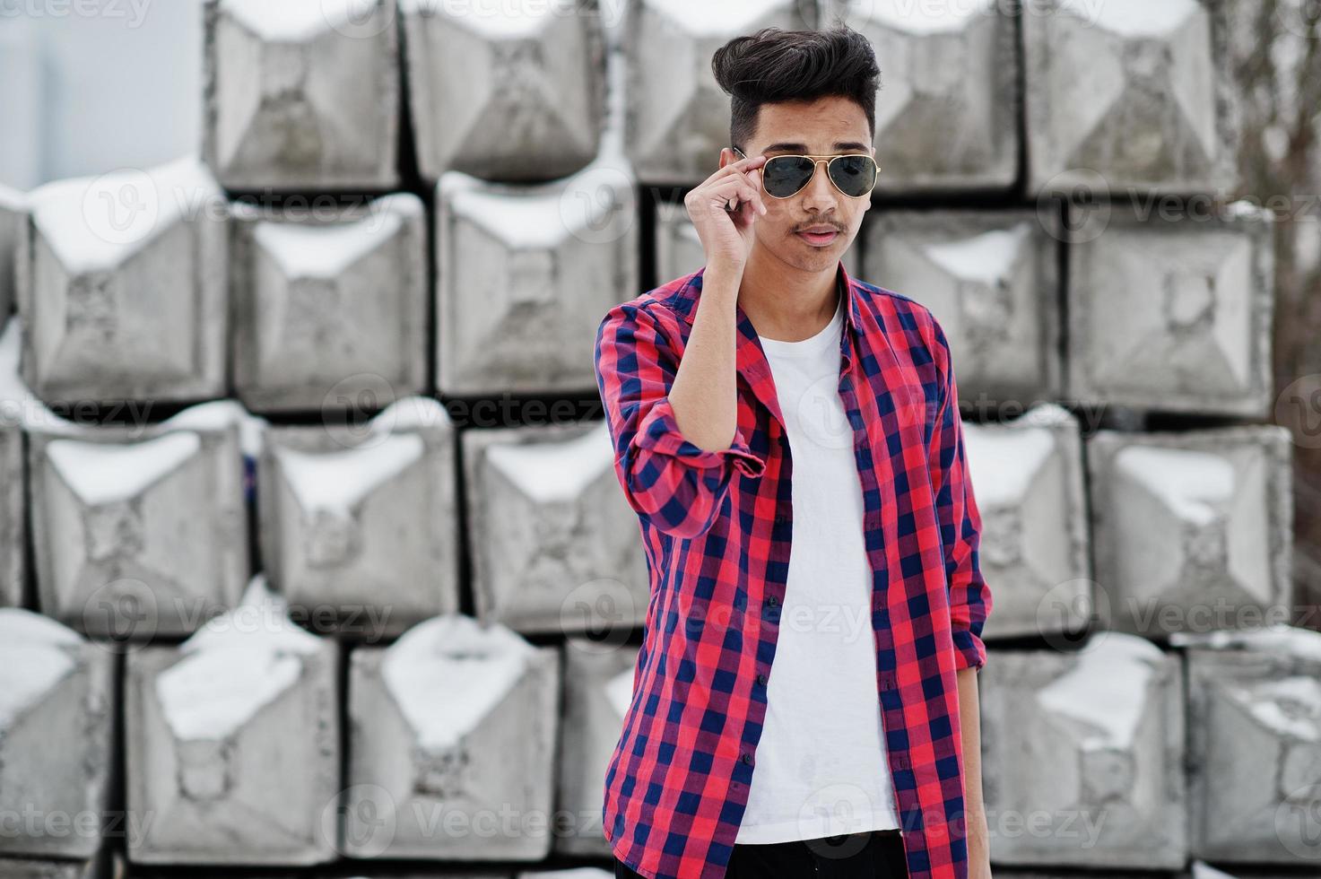 Un joven indio casual con camisa a cuadros y gafas de sol posó contra bloques de piedra. foto