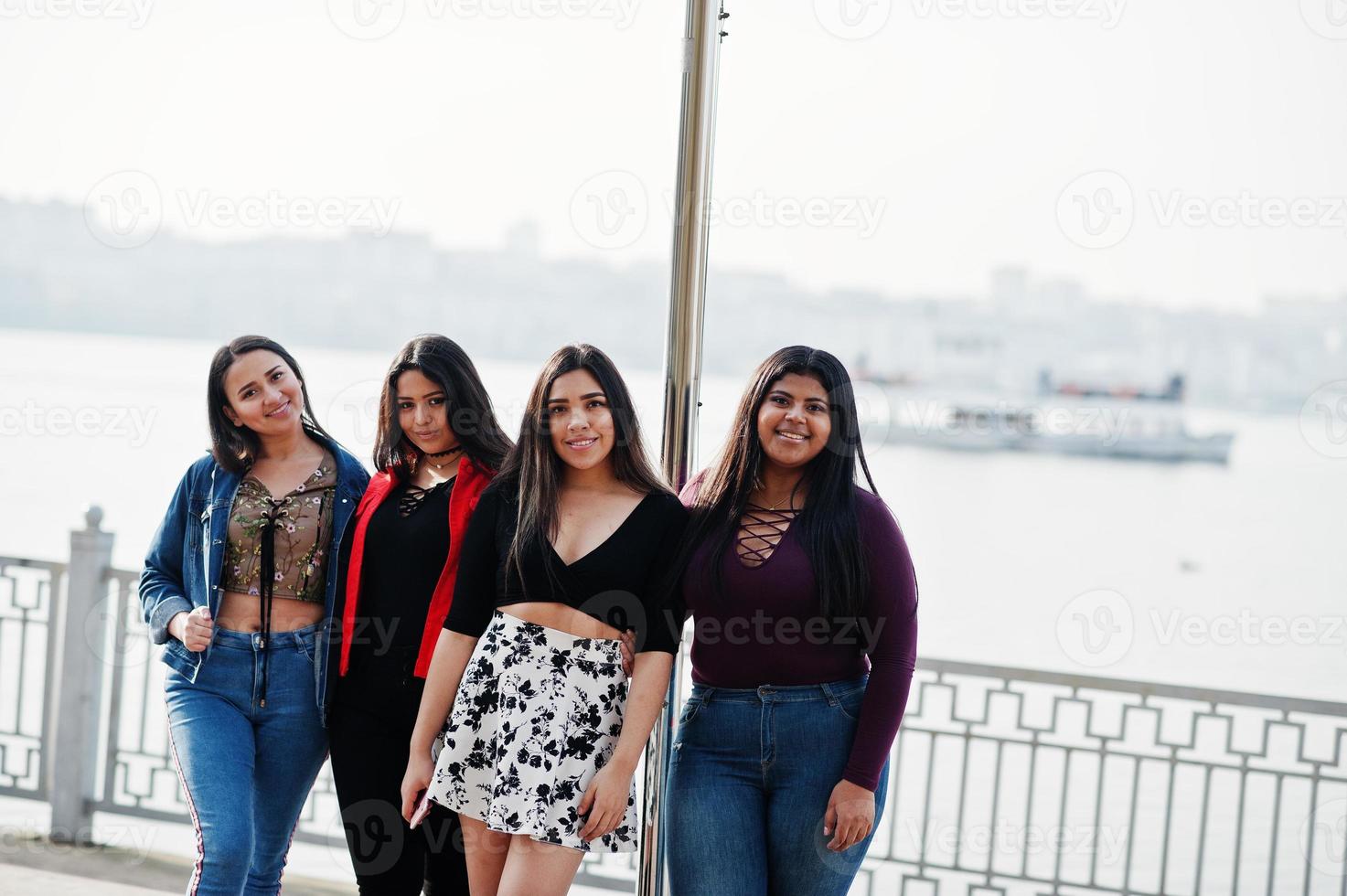 Group of four happy and pretty latino girls from Ecuador posed against lake with ferry. photo