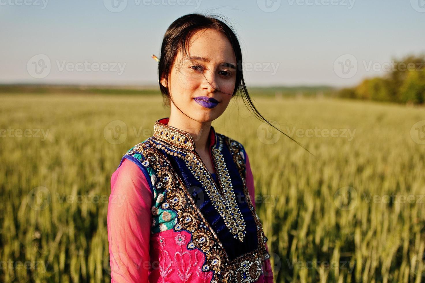 tierna niña india en sari, con maquillaje de labios violetas posada en el campo al atardecer. modelo indio de moda. foto