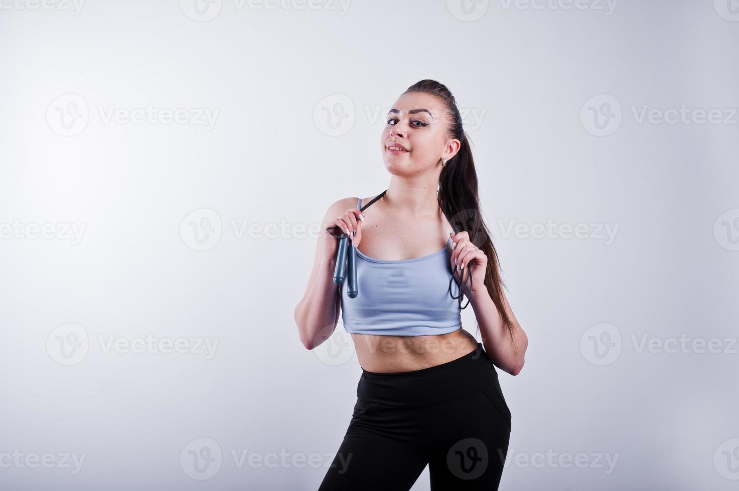 alegre y atractiva mujer joven en forma con polainas superiores y negras con cuerda para saltar aislada sobre fondo blanco. foto