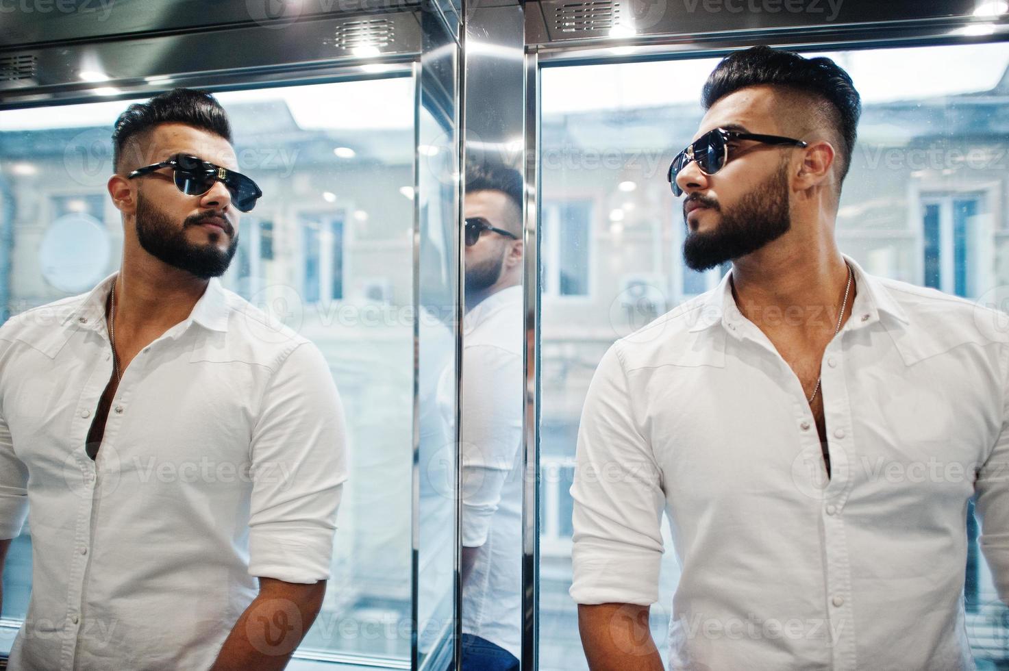 Stylish tall arabian man model in white shirt and sunglasses posed at elevator inside. photo