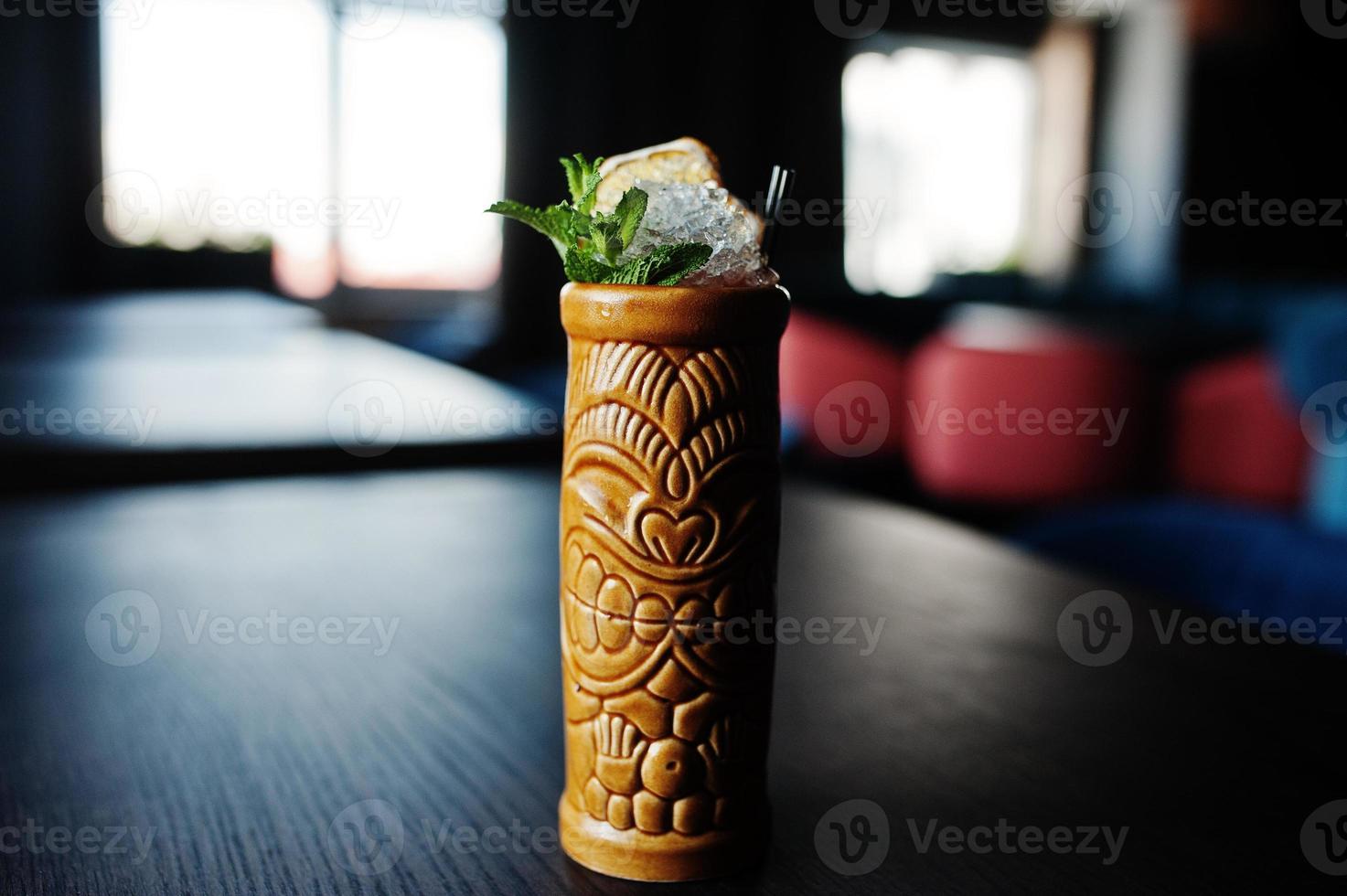 Alcoholic cocktail with mint in originally voodoo earthen glass on bar table. photo