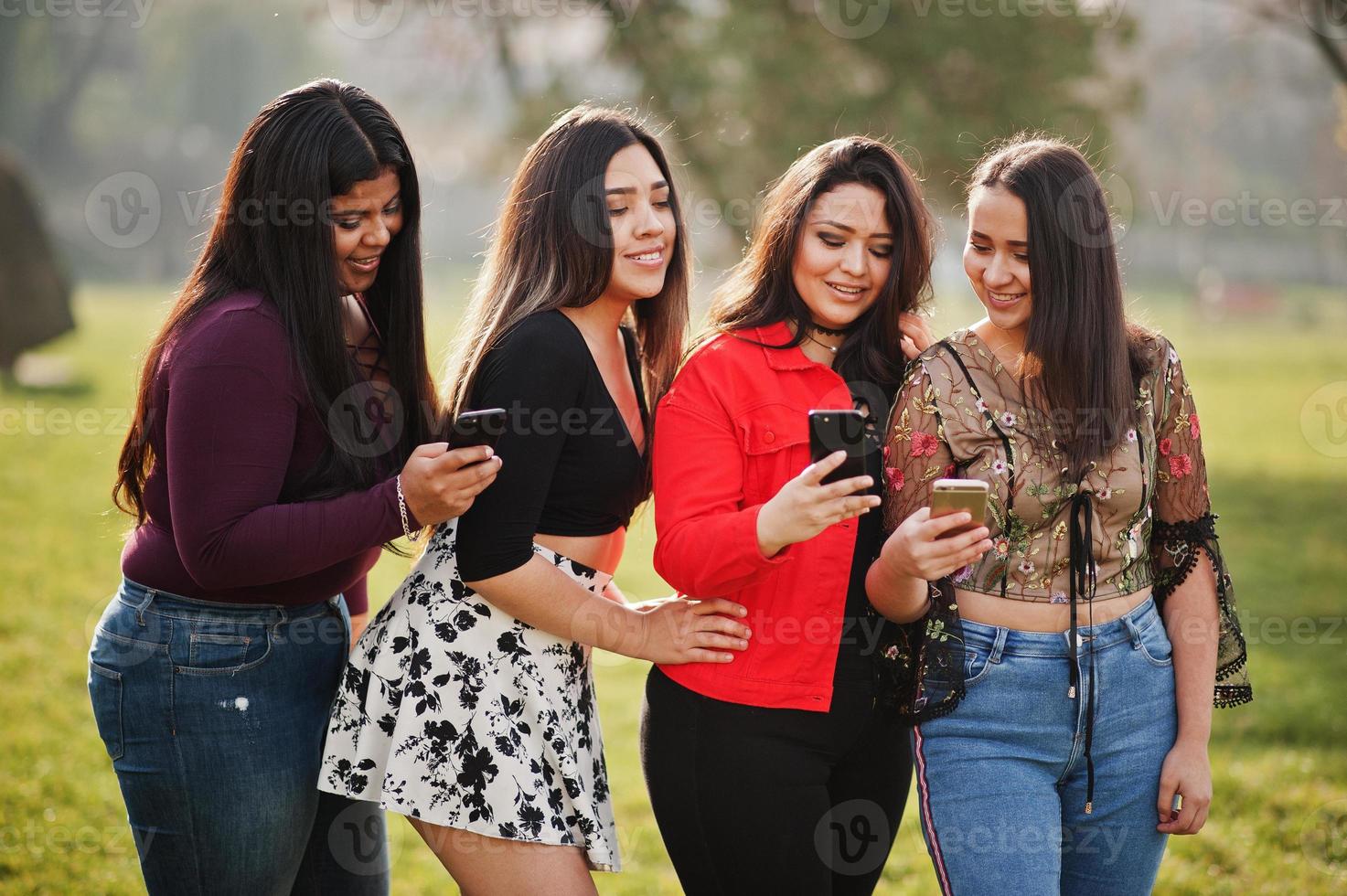 Group of four happy and pretty latino girls from Ecuador posed at street and looking at mobile phones. photo